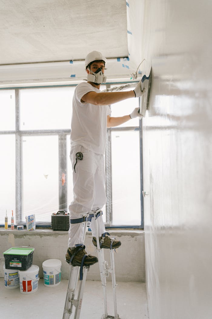 Construction worker smoothing a wall indoors using safety gear.