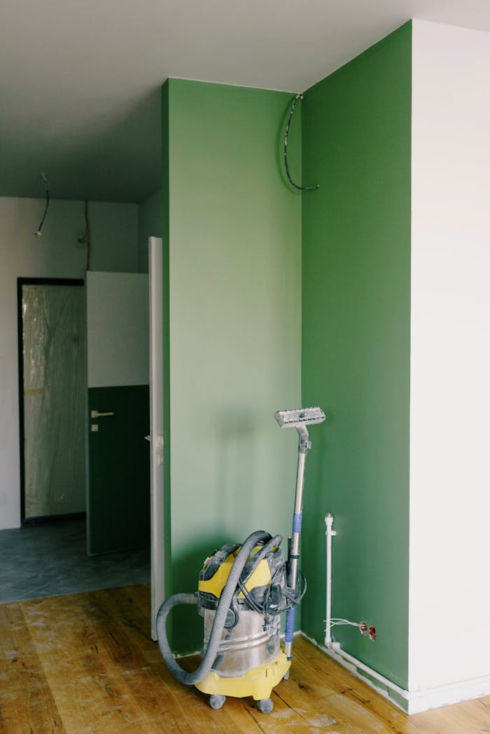 Building vacuum cleaner placed in corner of green painted room during renovation works in new apartment
